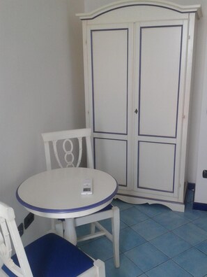 A room with a white table and chair, a cabinet with two doors, and a tiled floor. - Il Porticciolo di Amalfi (Amalfi)
