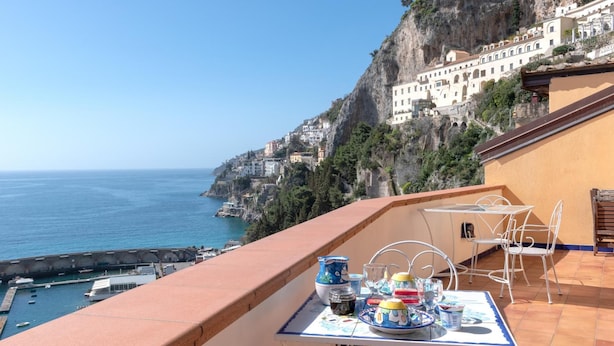 Une terrasse avec une table dressée pour le dîner, offrant une vue sur une ville côtière avec des bâtiments perchés sur une falaise.