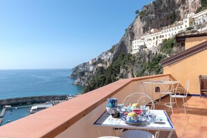 Une terrasse avec une table dressée pour le dîner, offrant une vue sur une ville côtière avec des bâtiments perchés sur une falaise.
