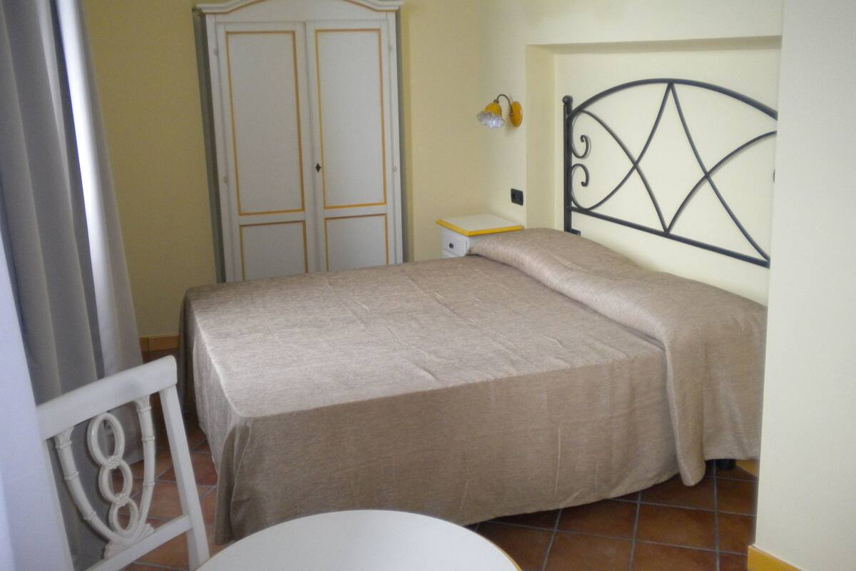 Un dormitori amb un llit, un armari, una taula de nit i una cadira.