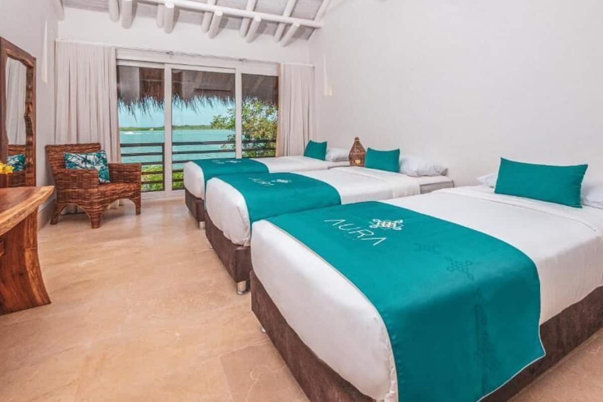 A hotel room with two beds, a wooden chair, a small table, and a view of the sea through a sliding door.