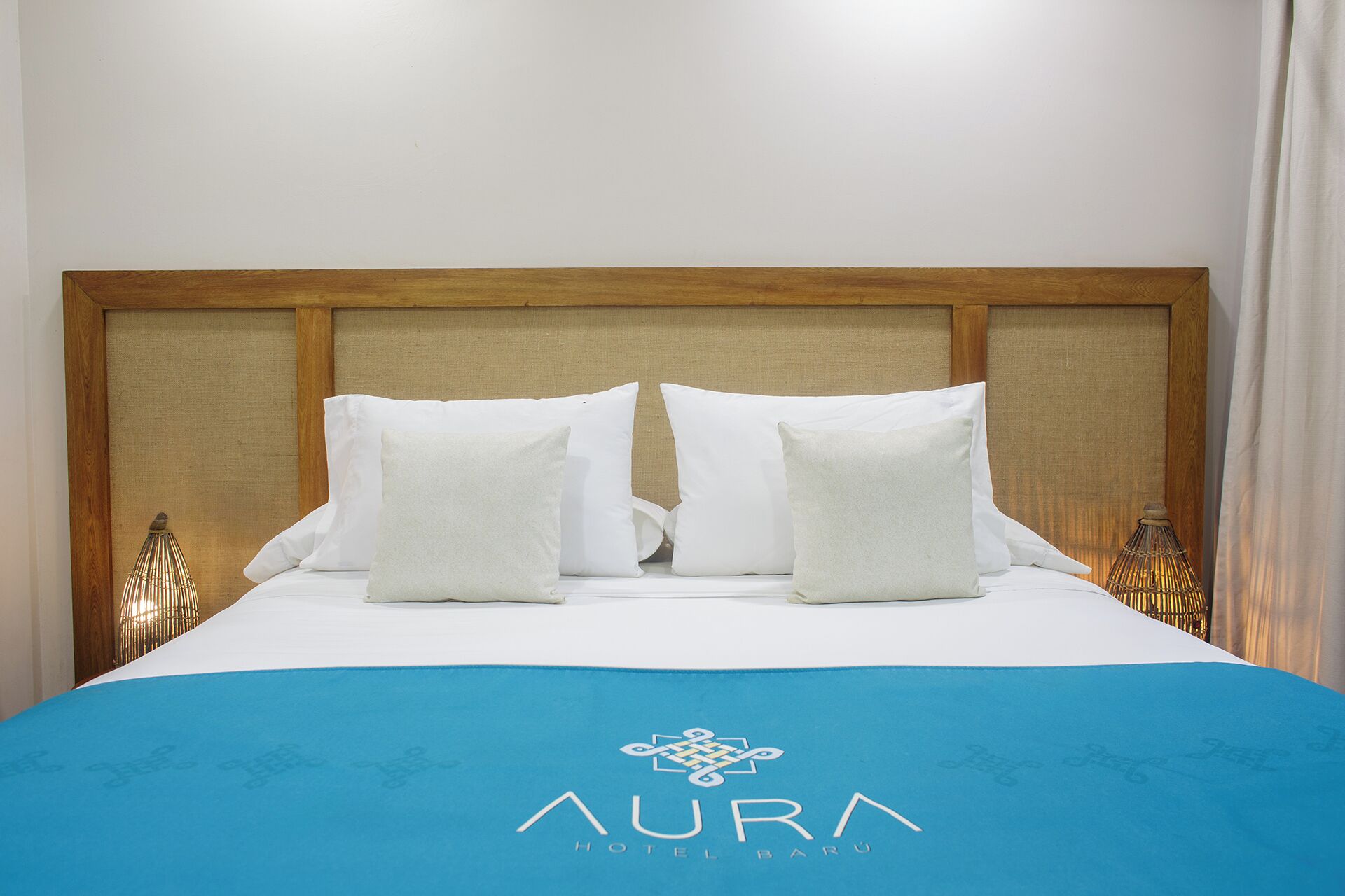 A hotel room with a wooden headboard, white bedding, and a blue bedspread with the hotel logo.