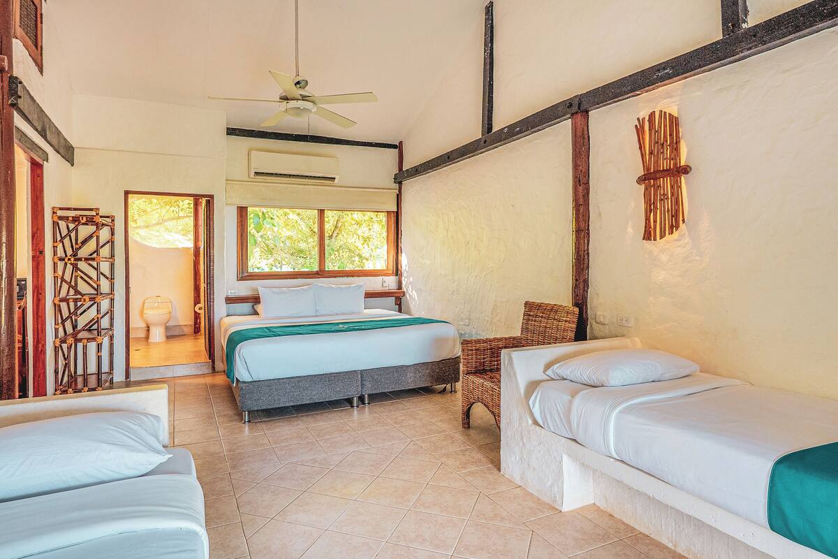 A room with a bed, two bedside tables, a window, a ceiling fan, and a door leading to a bathroom.