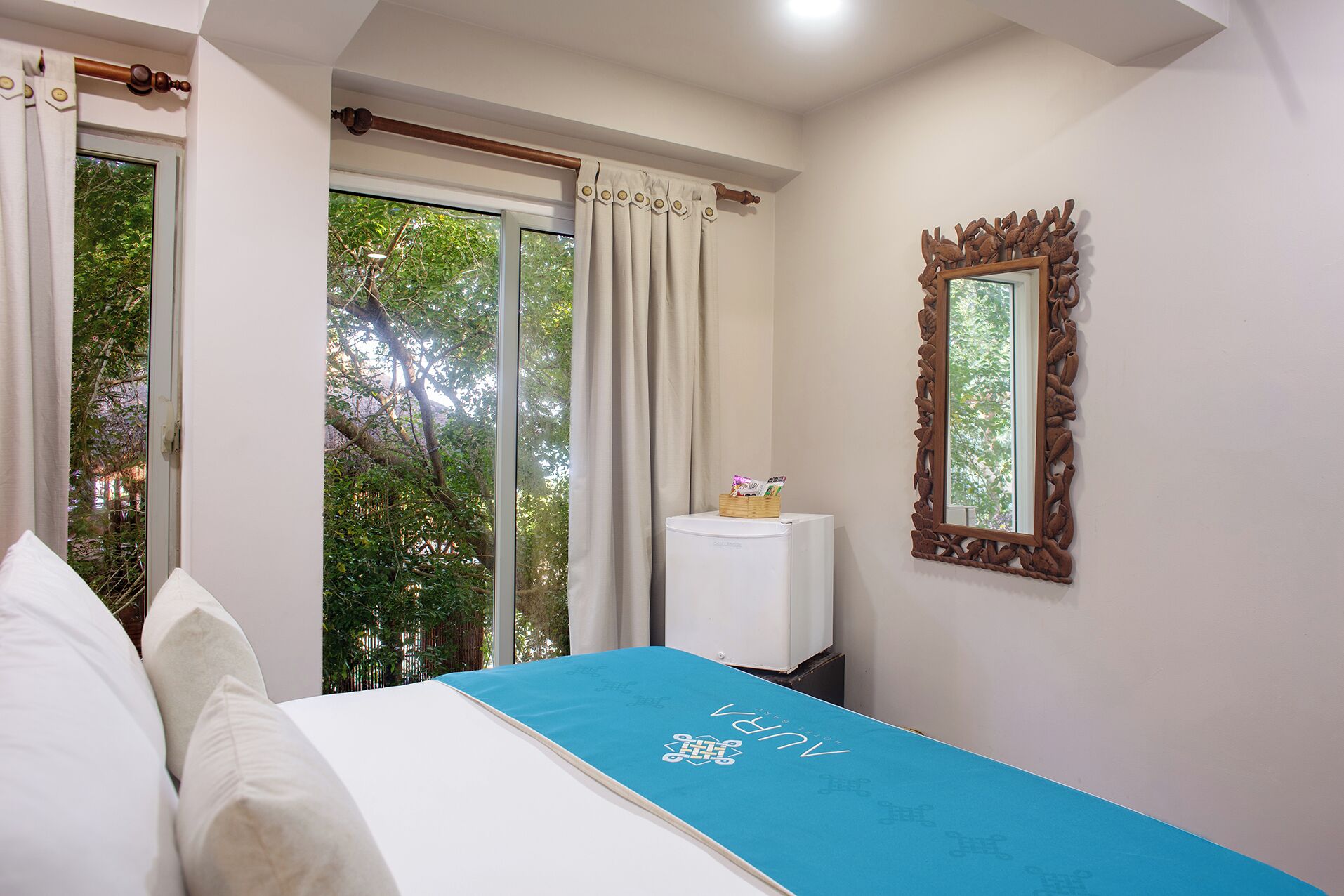 A bedroom with a bed, a small table with a basket, a mirror, and a window with curtains.
