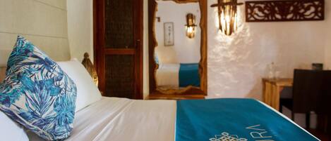 Una habitación de hotel con una cama, una colcha azul con la palabra "NURN", una puerta de madera y una lámpara fijada a la pared.