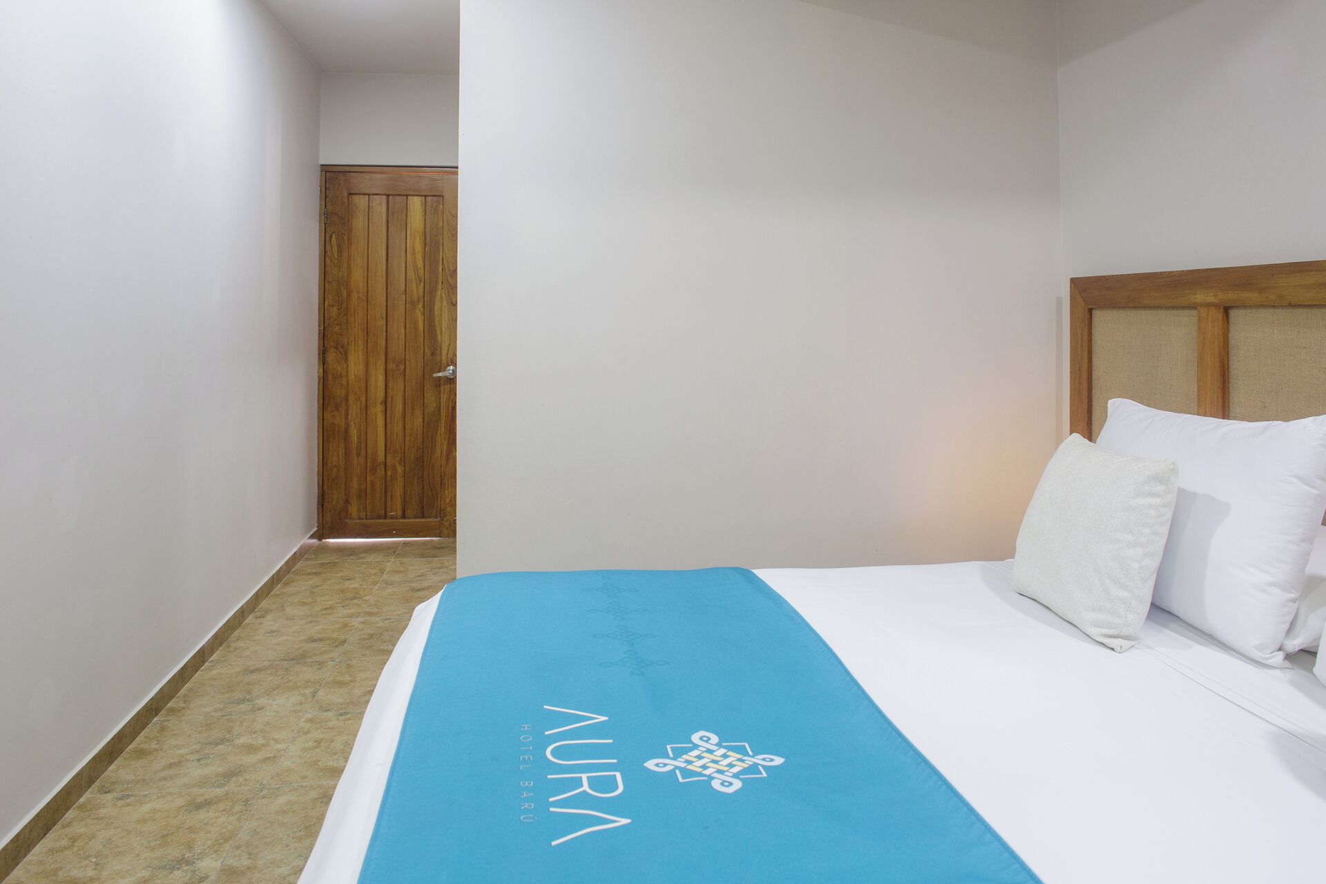 Ein Hotelzimmer mit Bett, Holztür und blauer Bettdecke mit dem Namen des Hotels.