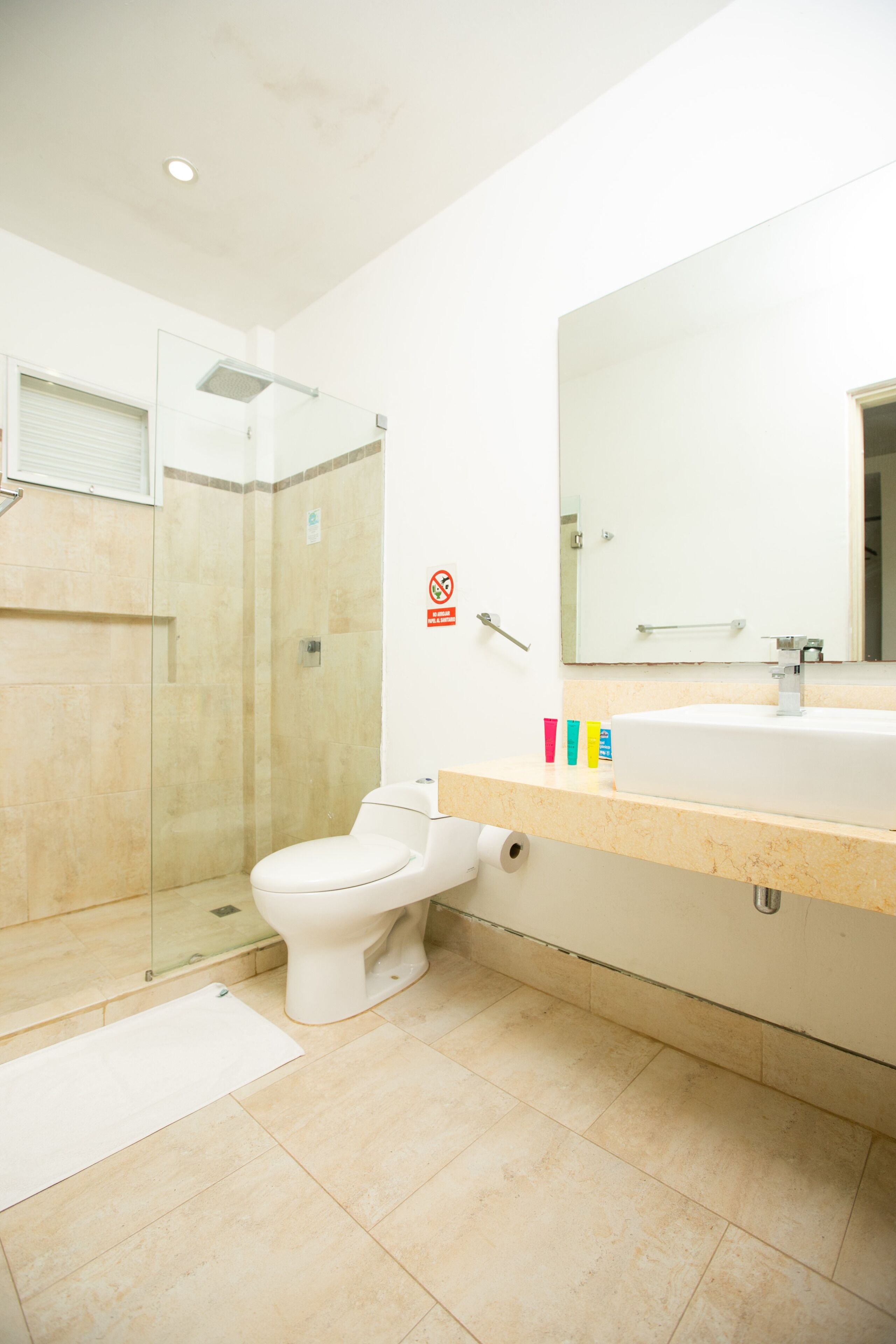 Et moderne badeværelse med en brusekabine i glas, et hvidt toilet og et gulv med beige fliser.