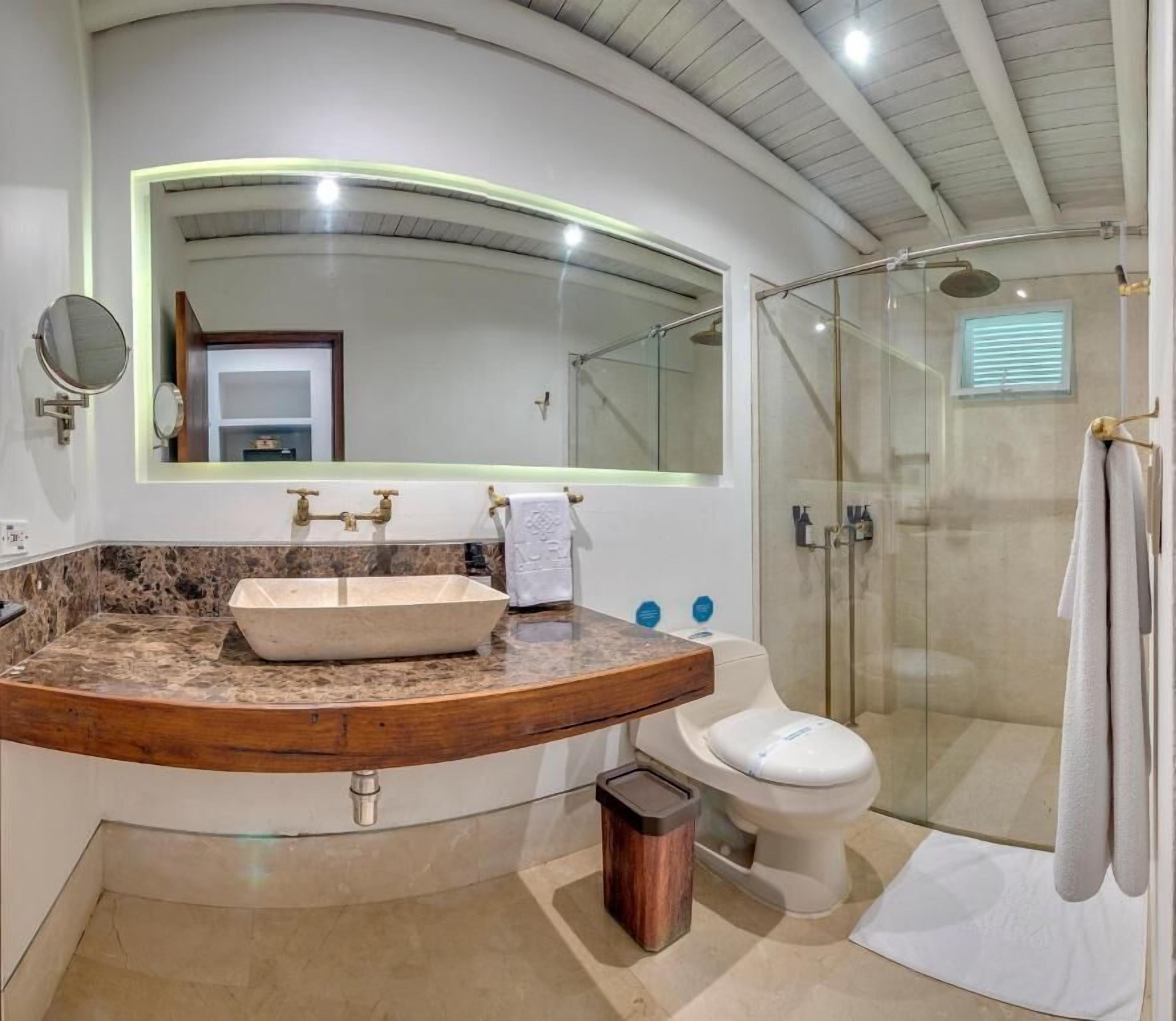 Un baño moderno con un tocador curvo, un espejo grande, una cabina de ducha de vidrio y un inodoro.