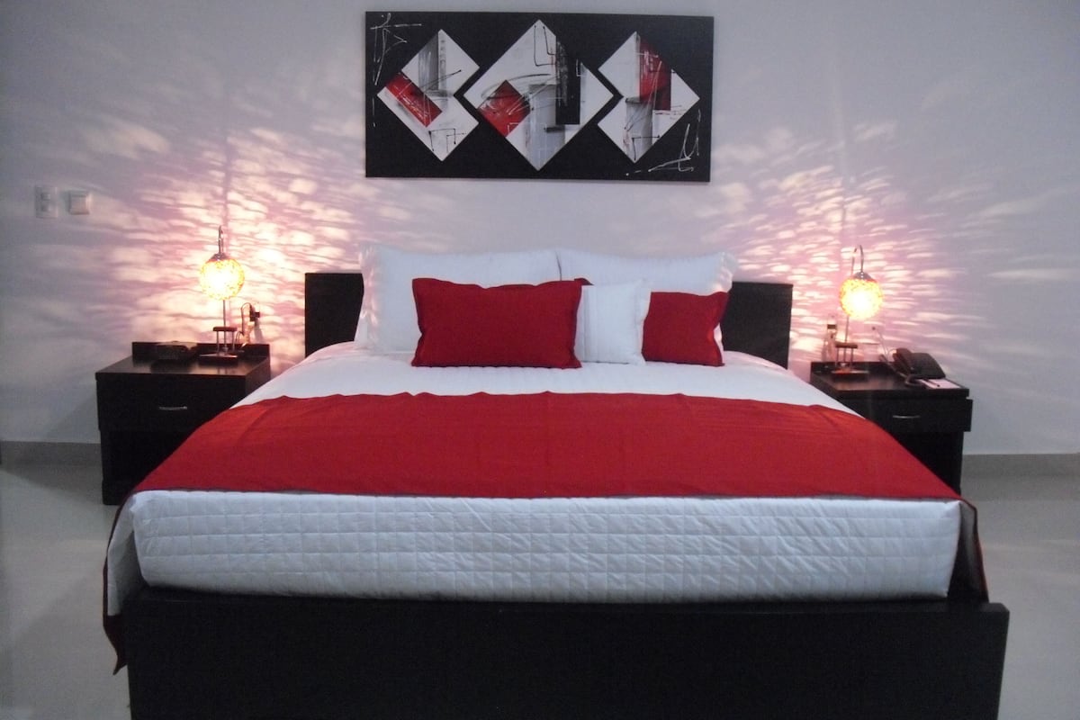 A bed with a red and white bedspread, two nightstands with lamps, and a wall art piece above the bed.