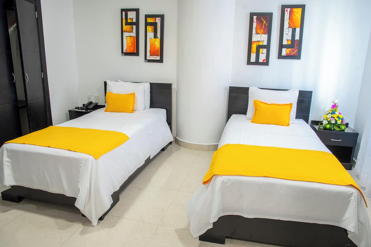 Two adjacent beds with white bedding and yellow accents, a nightstand with a phone, and abstract art on the walls.