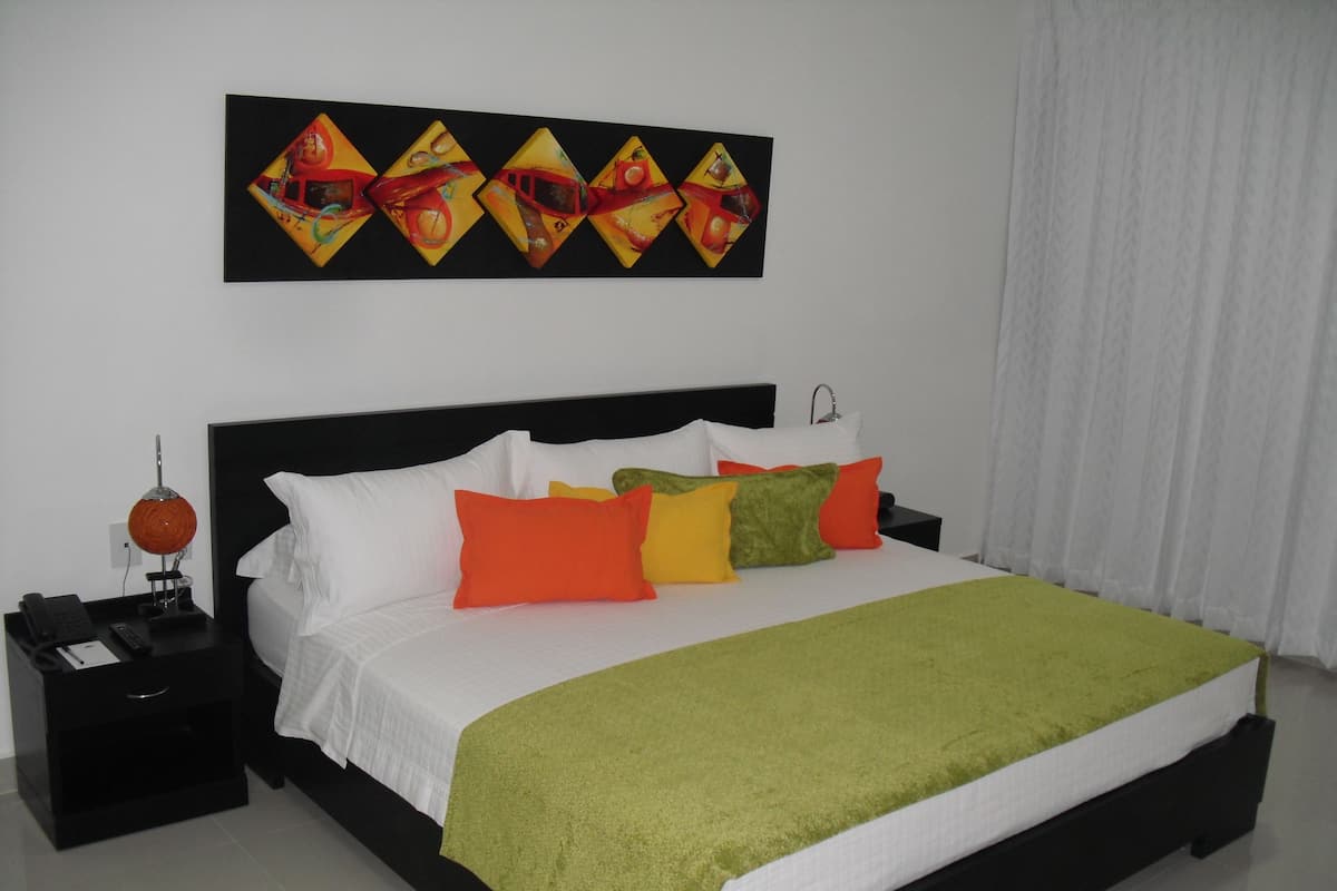 A hotel room with a large bed, a nightstand, a lamp, and a wall art piece.