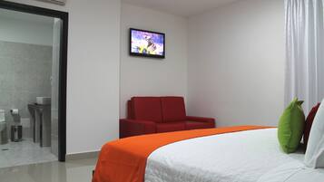 A hotel room with a bed, a TV, a red chair, and a bathroom visible through an open door.