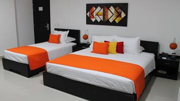 A hotel room with two beds, each with an orange bedspread and white pillows. There is a black nightstand with a lamp and a small table with a phone and a book. A painting is on the wall above the beds.