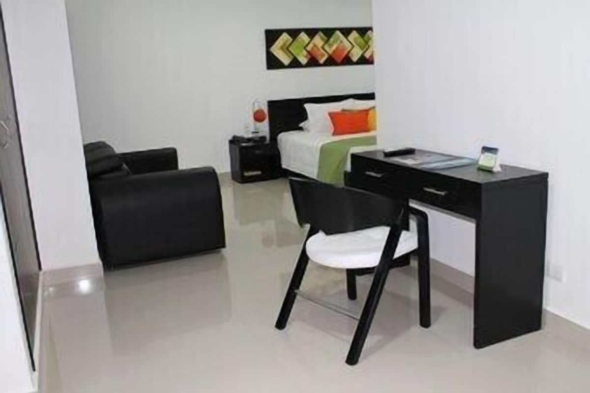 A room with a bed, a desk, a chair, and a small table.