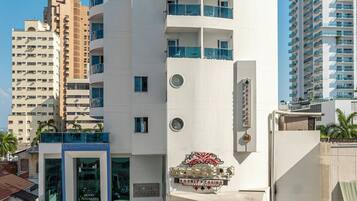 Hotel Atlantic features a curved facade with balconies and a rooftop terrace with seating and palm trees.