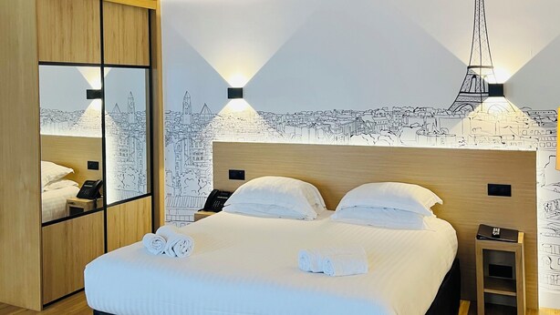 Un hotel moderno con una cama grande, vigas de techo de madera, un mural con vista a la ciudad y vistas a la Torre Eiffel.
