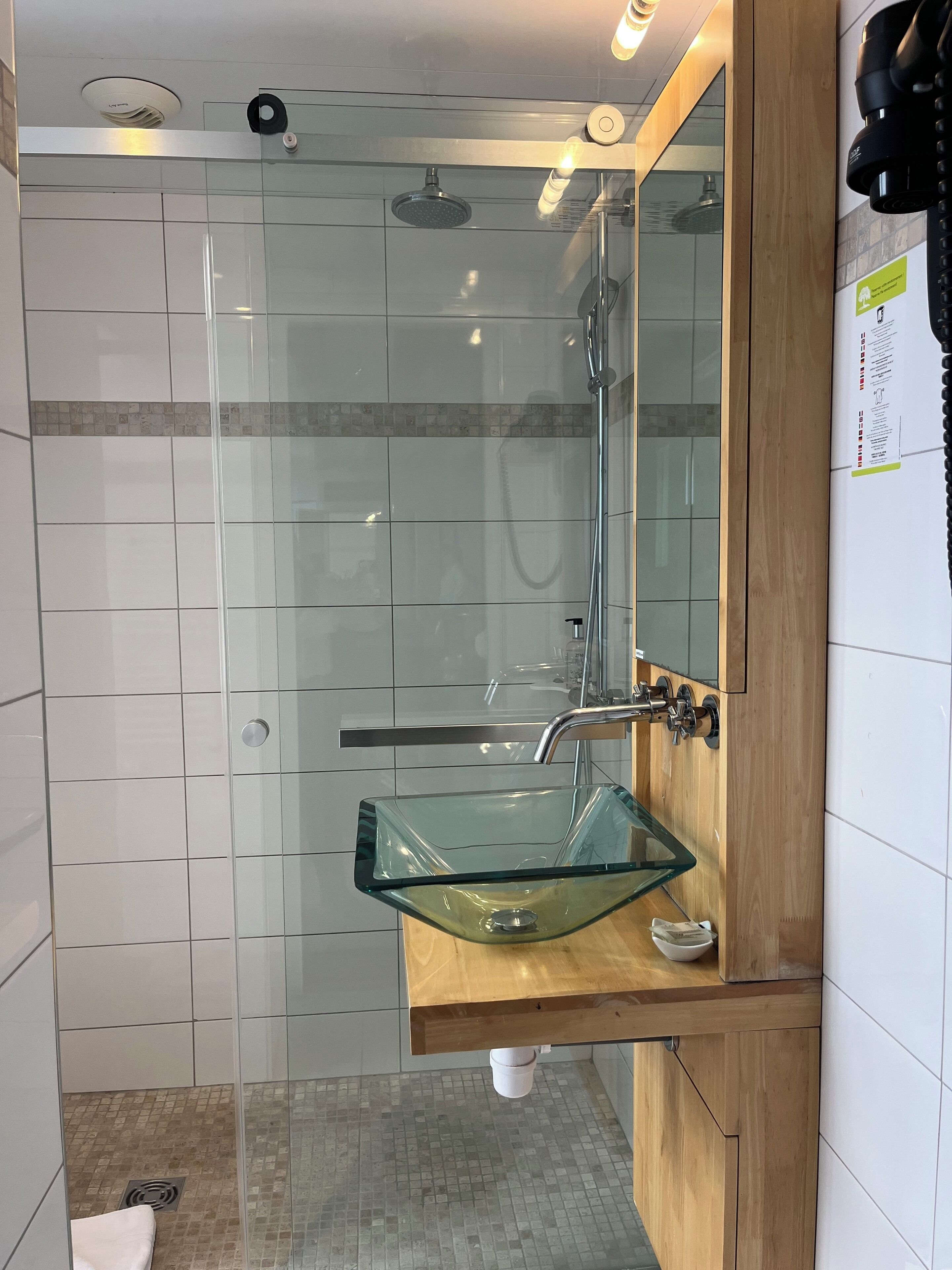 Ein modernes Badezimmer mit einem Glaskonstruktionsbecken, einem Holzkosmetikschrank, einer Glasdusche und einem Spiegel mit schwarzem Griff.