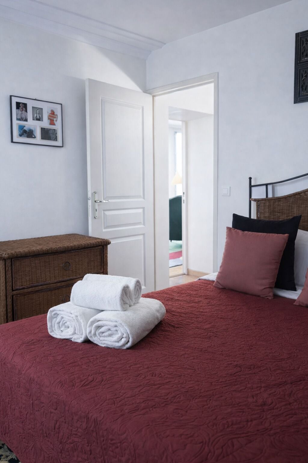 A bedroom with a red bedspread, a wooden dresser, and a white door.