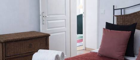 A bedroom with a red bedspread, a wooden dresser, and a white door.