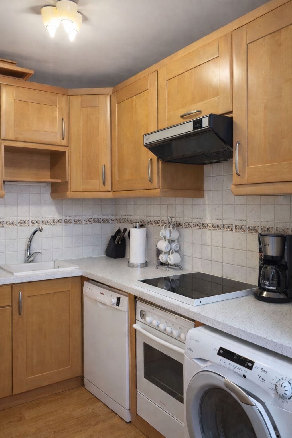 Uma cozinha compacta com armários de madeira, lava-louças, forno, máquina de lavar, cafeteira e micro-ondas.