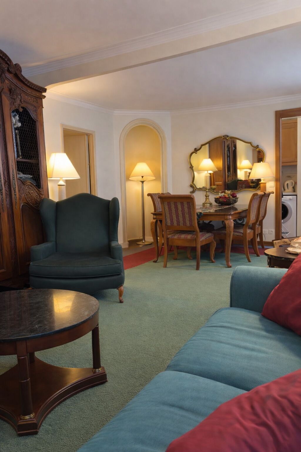 A living room with a green armchair, a round coffee table, a sofa, and a dining area with a table and chairs.