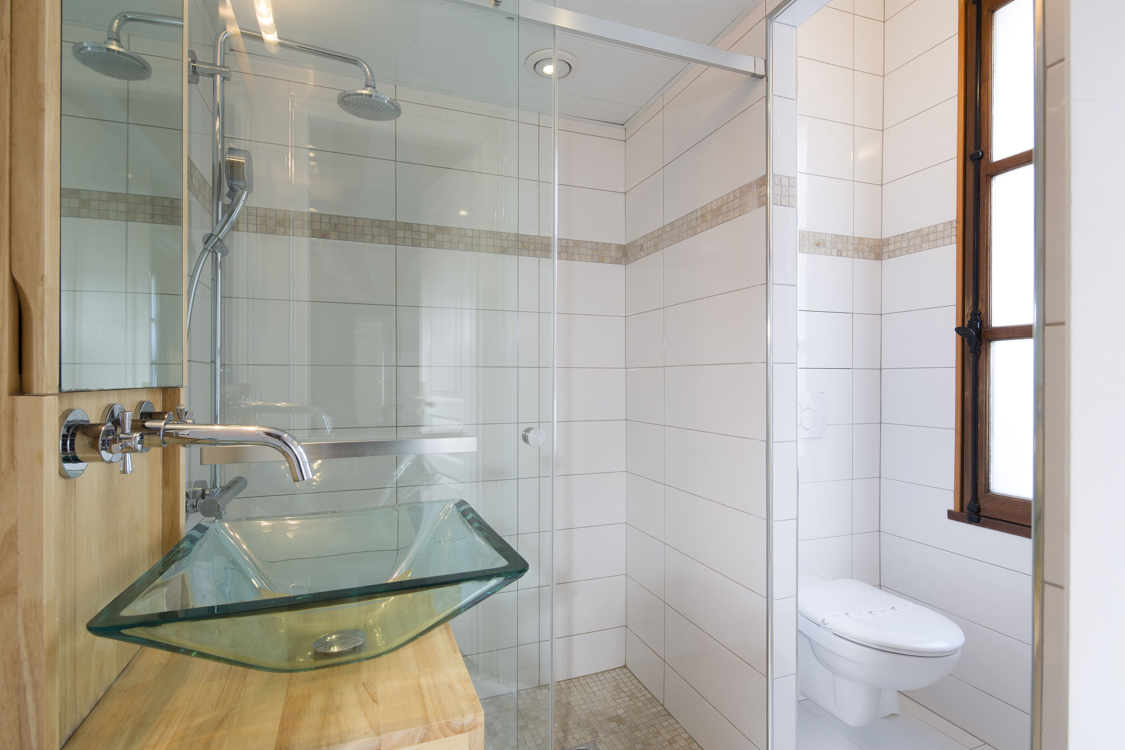 A modern bathroom with a glass sink, a shower, and a toilet.