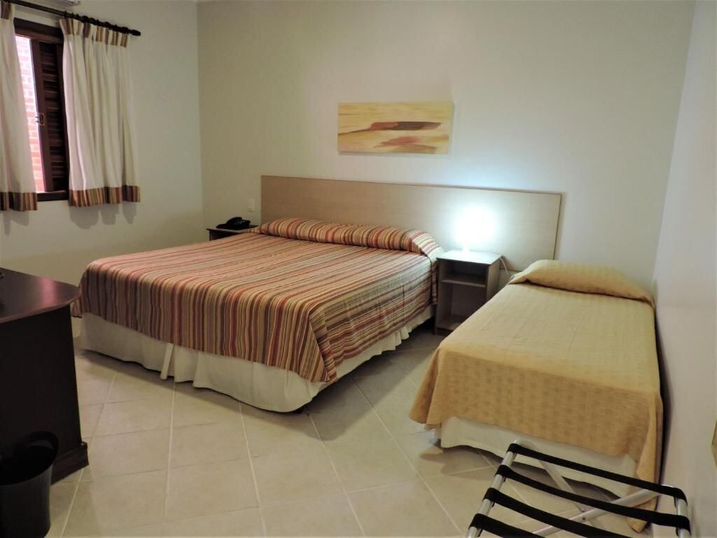 A hotel room with two beds, a desk, a chair, a nightstand, and a wall-mounted lamp.