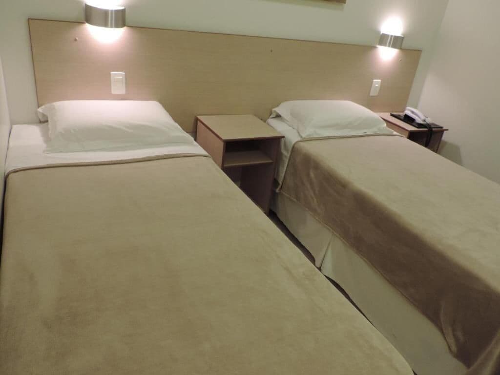 A hotel room with two beds, bedside tables, and wall-mounted lamps.