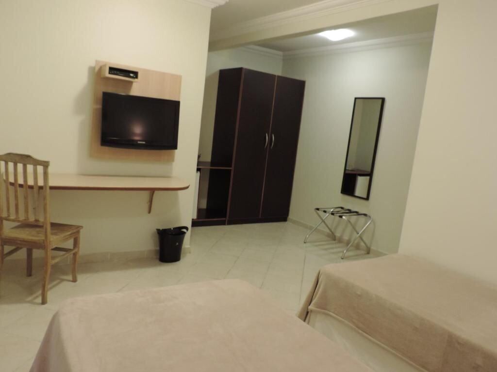 A bedroom with a bed, a chair, a TV mounted on the wall, a wardrobe, and a mirror.