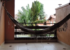A hammock hanging between two walls in a room with a tiled floor and a view of a large plant outside. - Hotel Costa Balena (Guarujá)