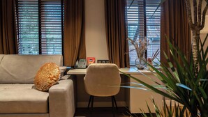 Een woonkamer met een bank, een bureau, een telefoon en een vaas met gedroogde planten.