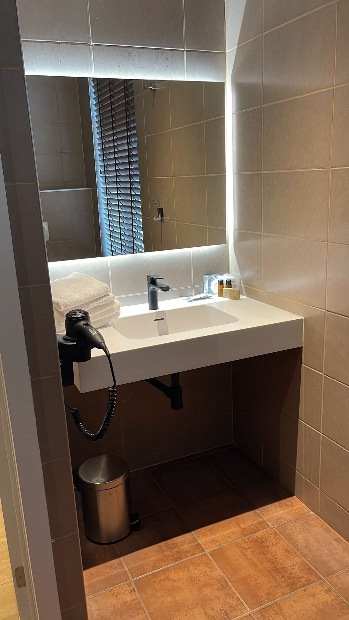 Een moderne badkamer met een witte wasbak, een handföhn en een prullenbak.