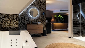 Een moderne badkamer met een groot bad, een ronde spiegel en een donkere mozaïektegelwand.