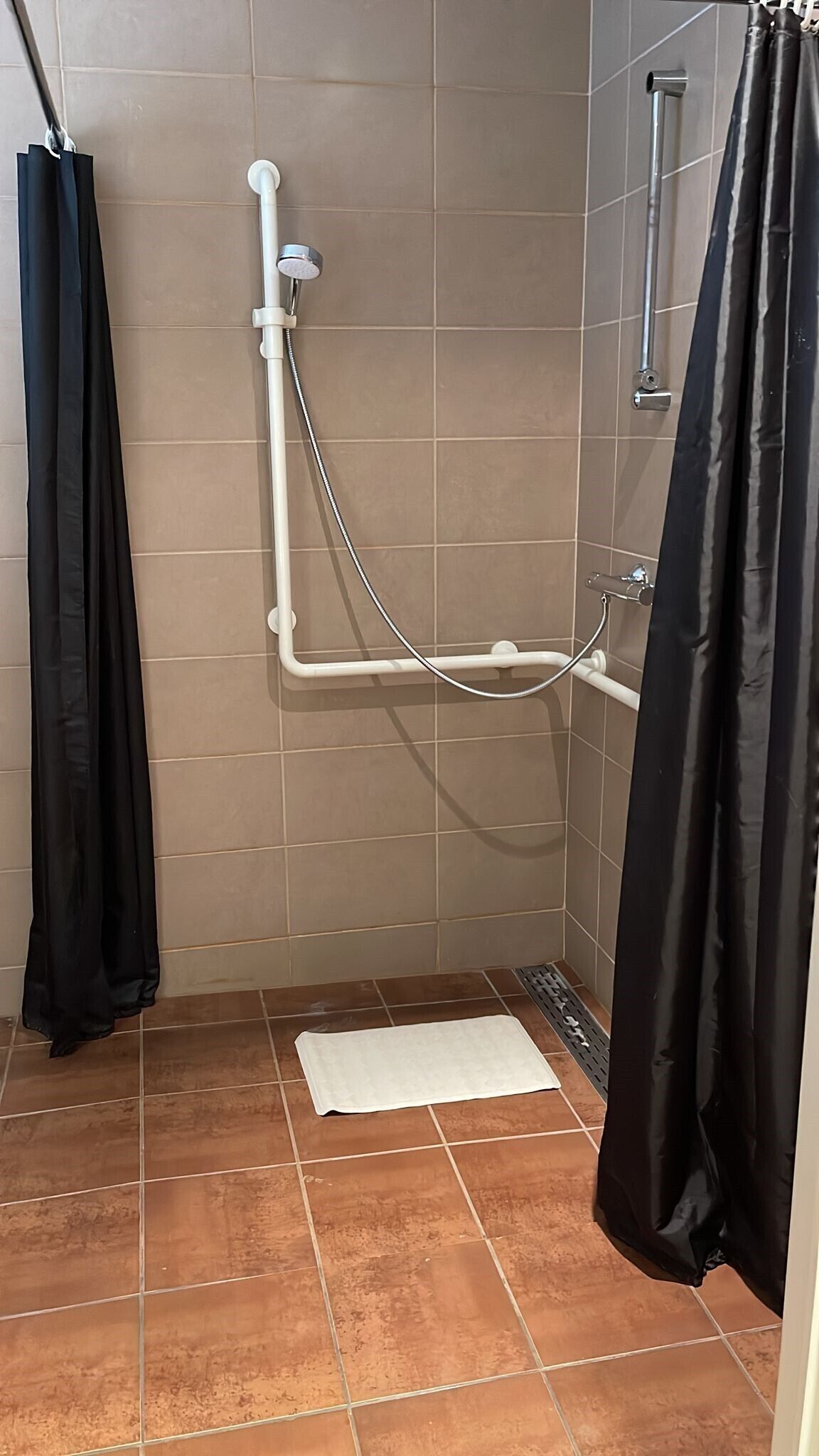 A shower area with a white showerhead, a black shower curtain, and a white mat on the floor.
