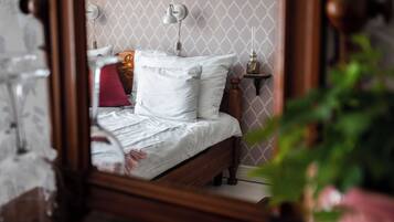 A bedroom with a wooden bed, white bedding, a bedside table with a lamp, and a wall-mounted mirror.