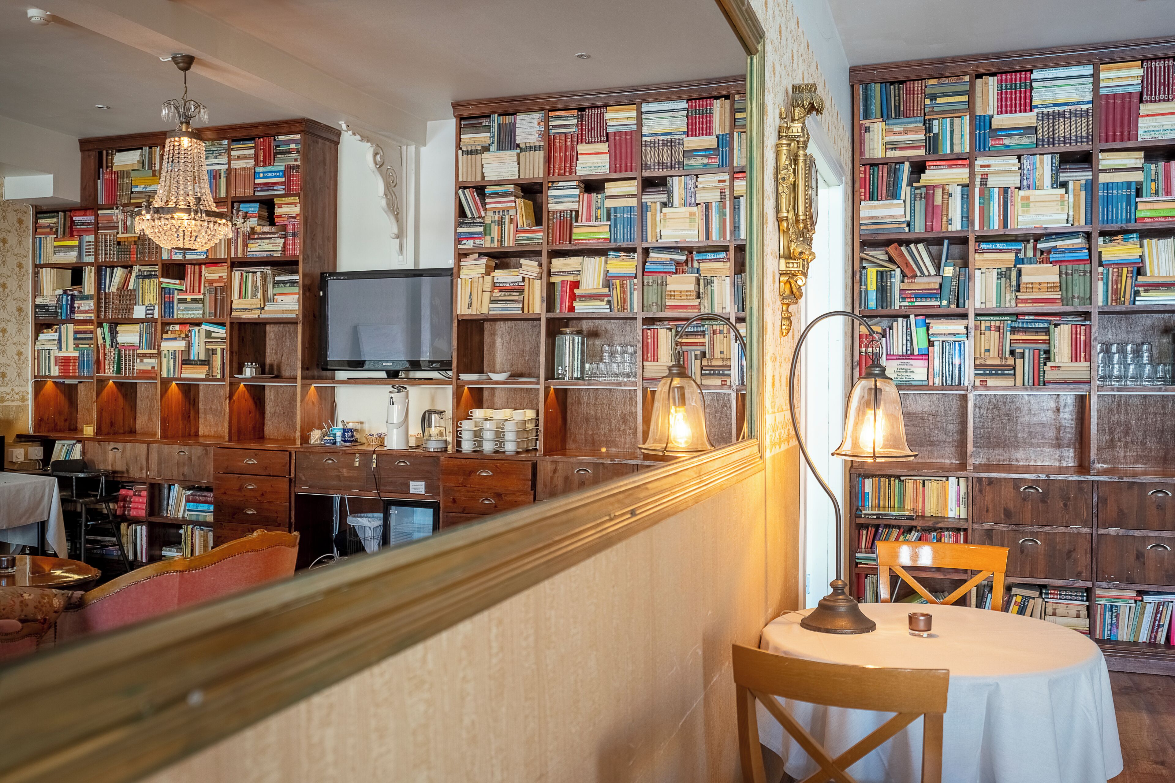 A library with bookshelves, a table, chairs, and a chandelier.