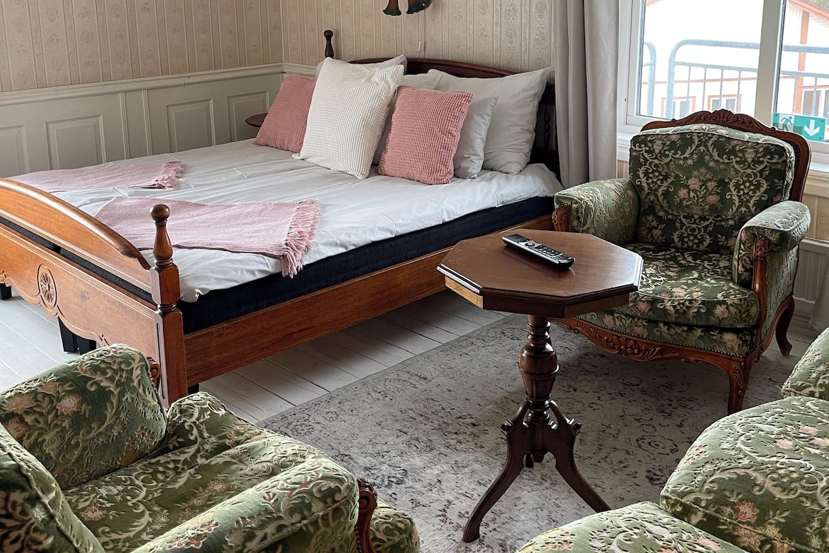 Une chambre à coucher avec un lit en bois, une table de chevet, un fauteuil vert et un canapé à motifs.