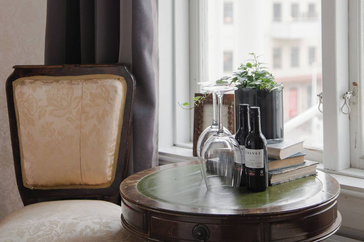 Une pièce avec une chaise, une petite table sur laquelle est posée une plante, et une fenêtre donnant sur des immeubles.
