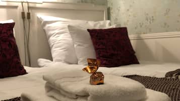 Cama bem arrumada com almofadas brancas e estampadas, uma toalha branca dobrada e um objeto decorativo sobre a cama.