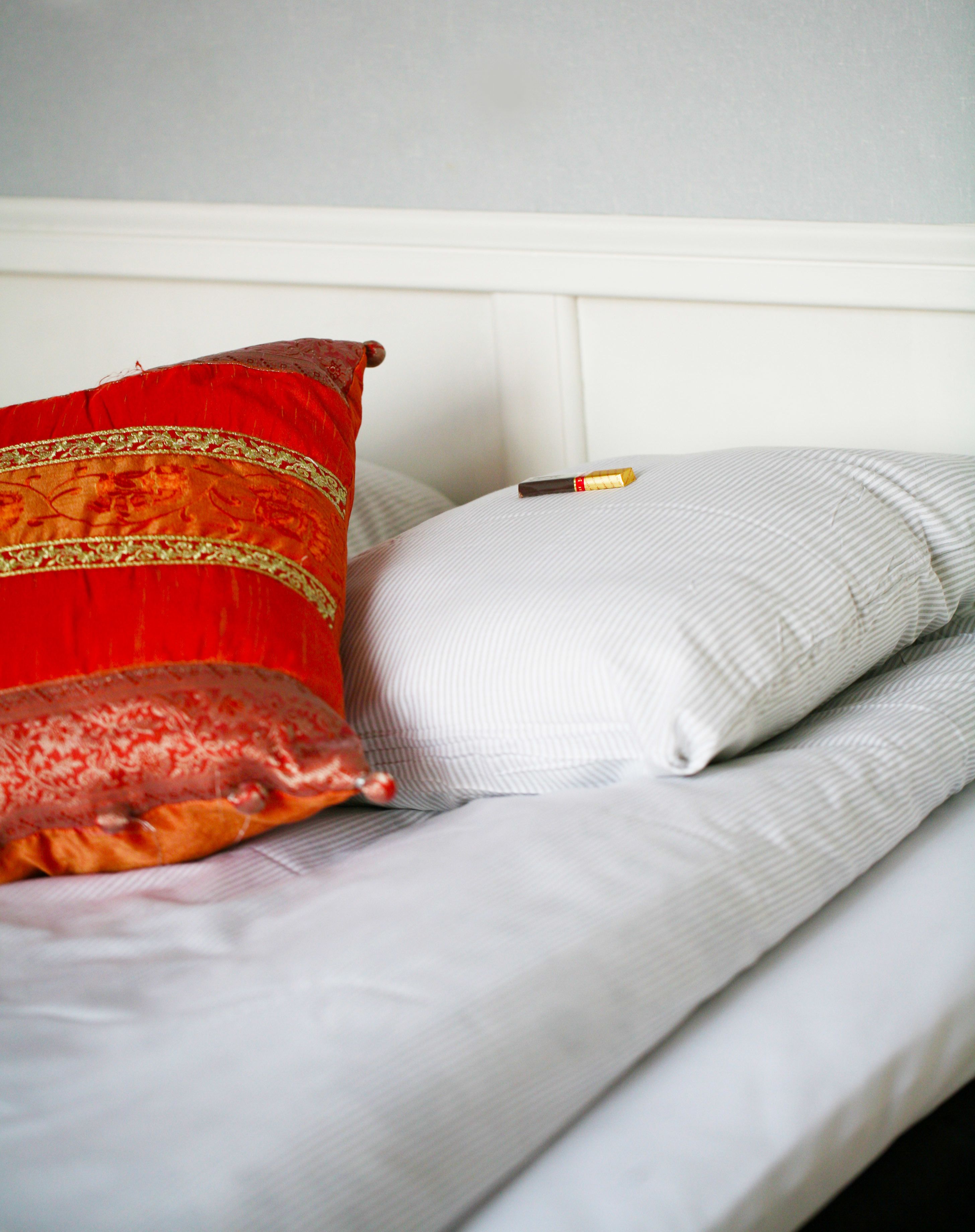 A bed with white bedding and two pillows, one red and one white.