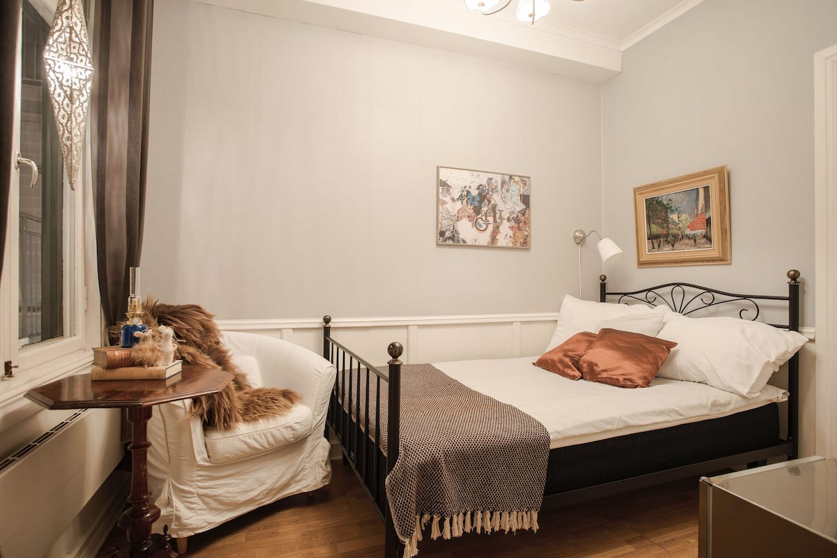 Une chambre à coucher avec un lit, une table de chevet avec une lampe, une chaise et une fenêtre avec des rideaux.