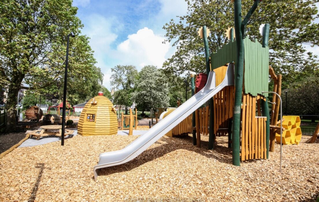 Ein Spielplatz mit Rutsche, Holzspielgeräten und einem Spielbereich im Bienenstock-Design.
