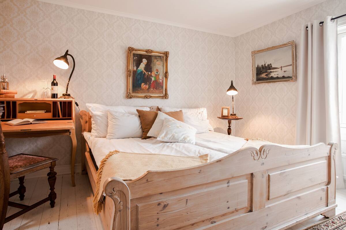 Une chambre à coucher avec un lit en bois, un bureau avec une lampe, une chaise et deux tableaux encadrés au mur.