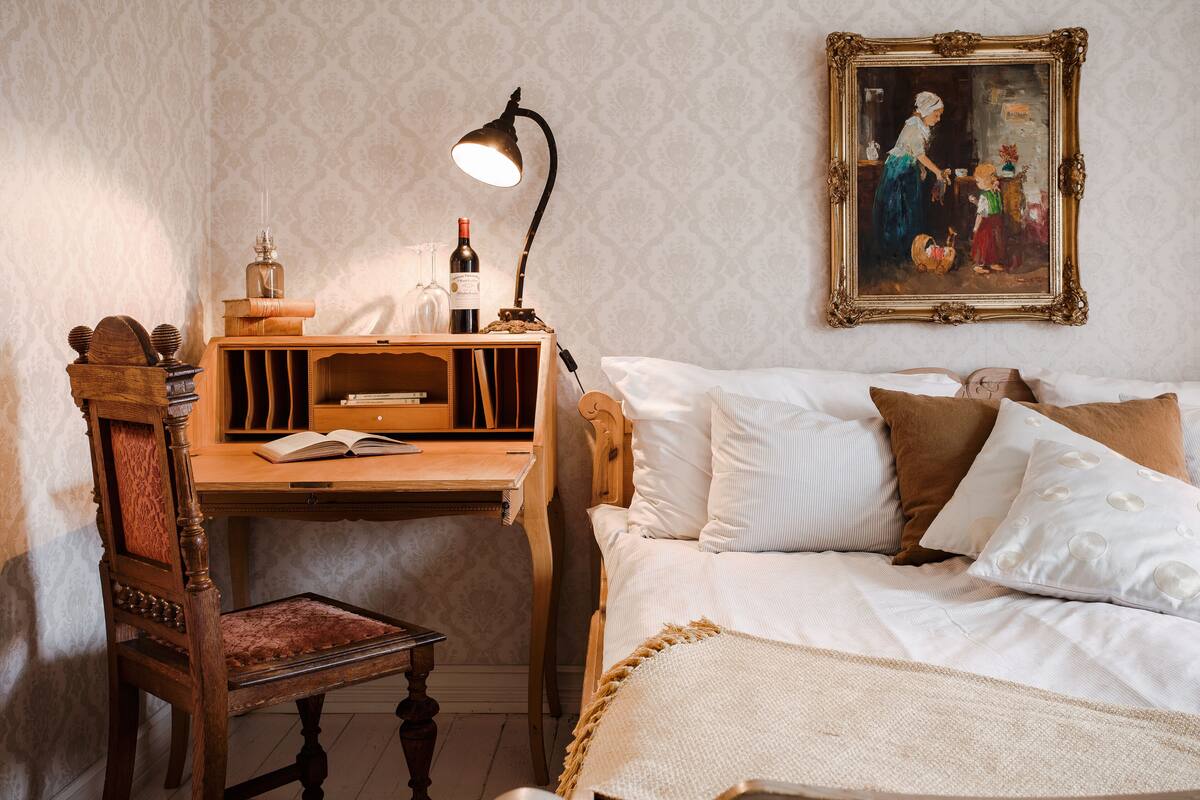 Une chambre avec un bureau en bois, une chaise, un lit avec une literie blanche et un tableau encadré au mur.