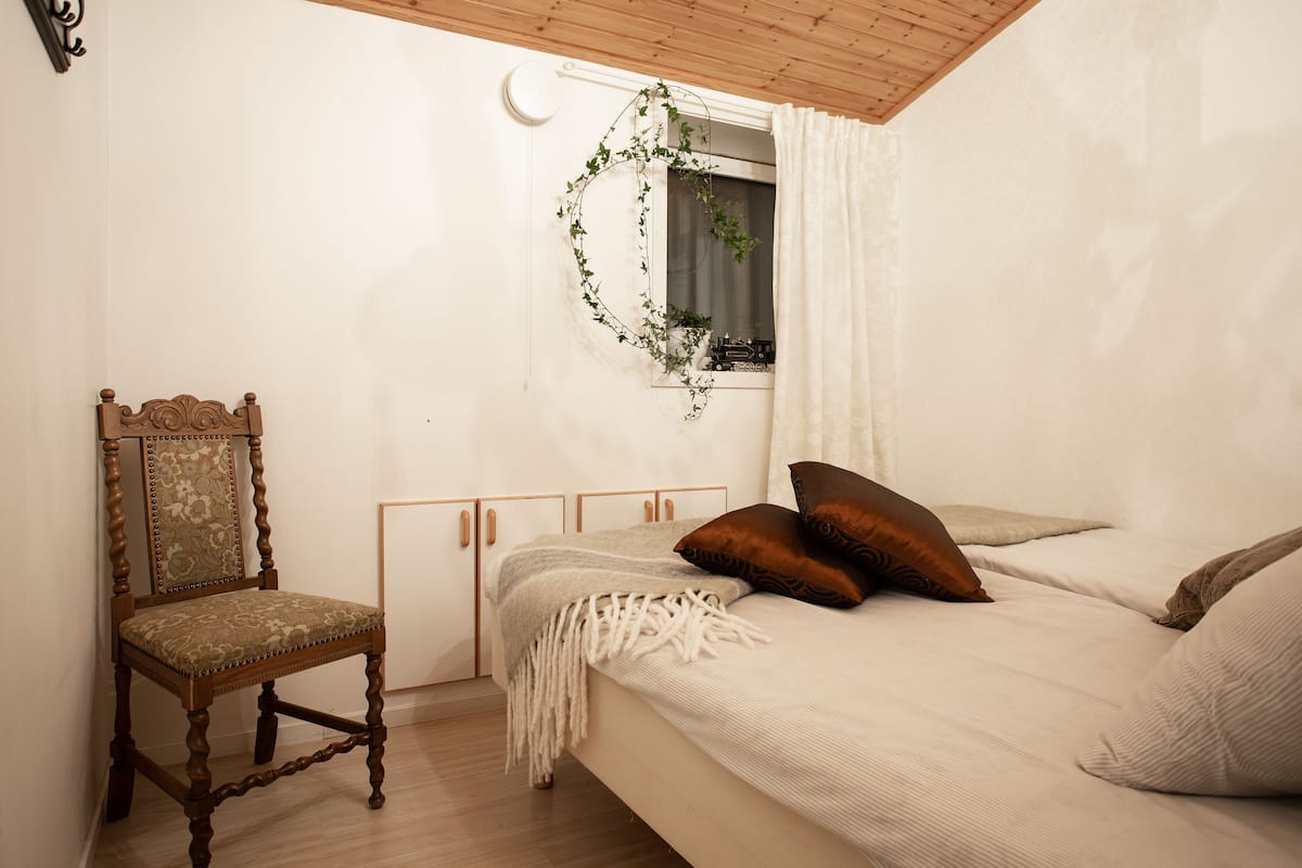 Une chambre à coucher avec un lit, une chaise, une fenêtre avec des rideaux et une horloge fixée au mur.