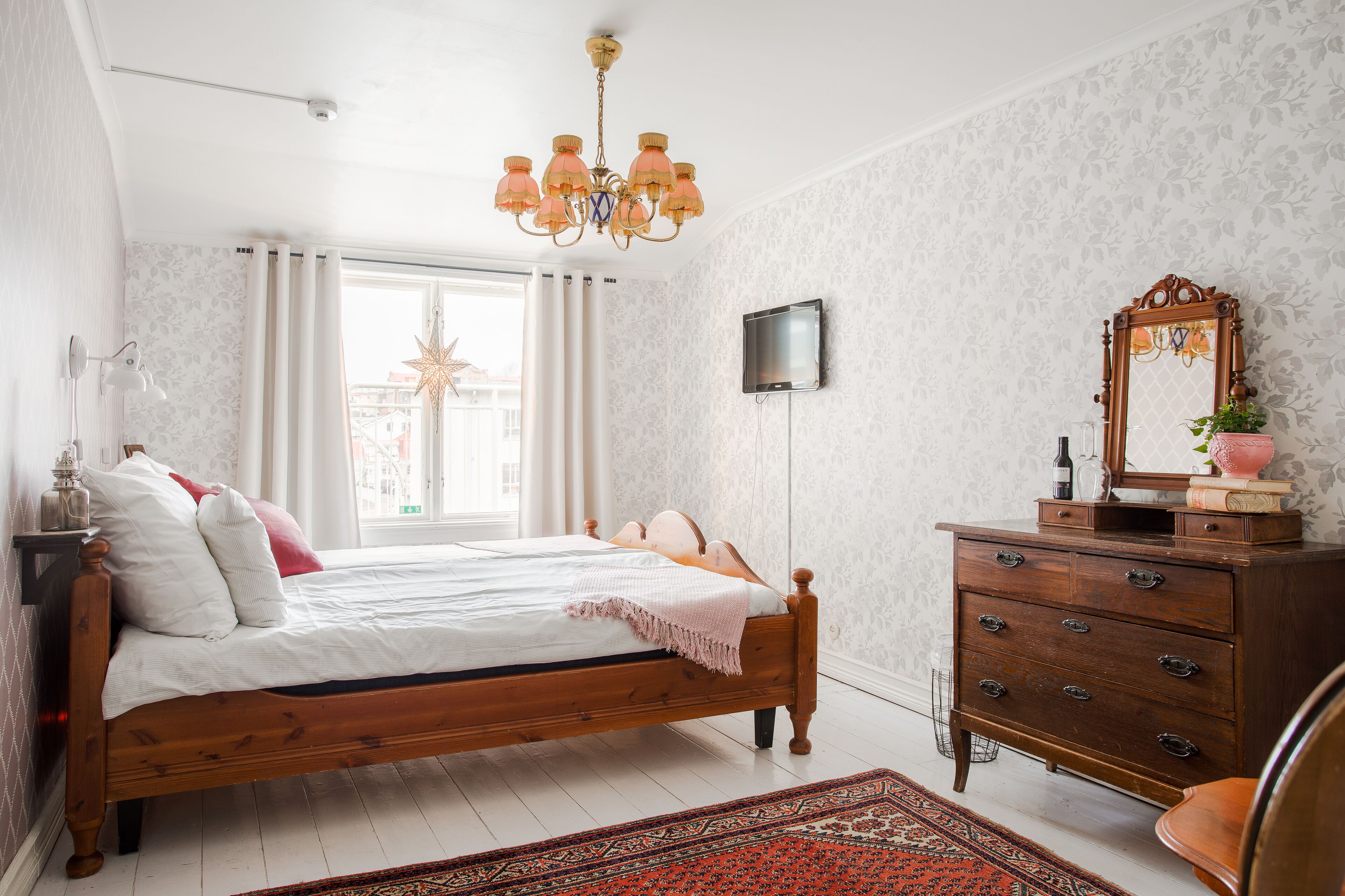 Quarto com cama de madeira, penteadeira, televisão e espelho decorativo.