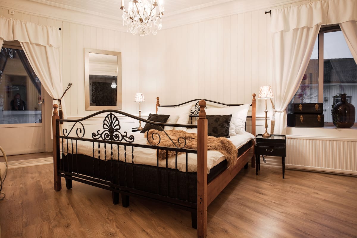 Une chambre à coucher avec un lit en bois, des rideaux blancs, un lustre et une fenêtre donnant sur un beau paysage.