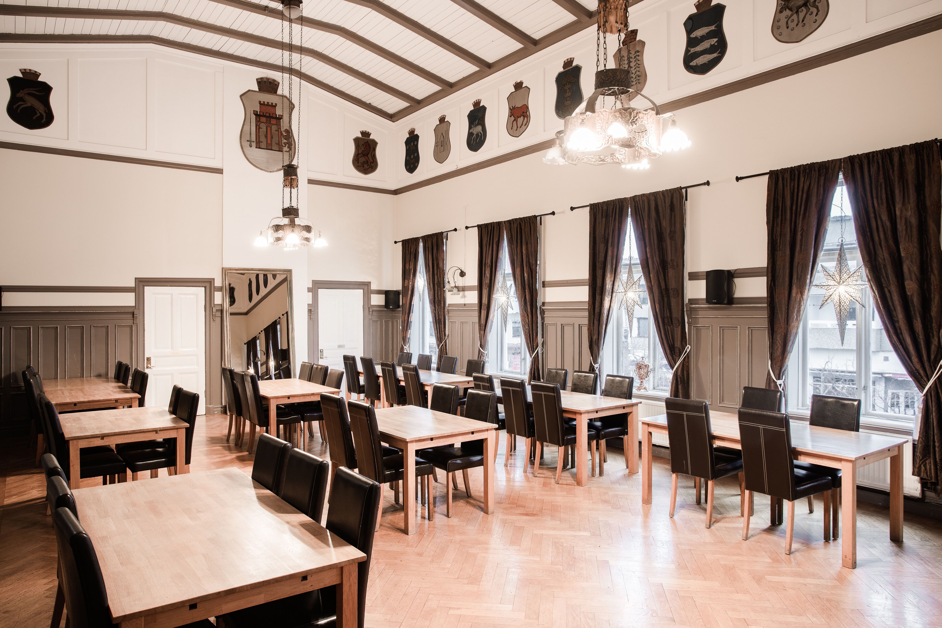 A dining area with multiple tables and chairs, wooden floors, and large windows with curtains.