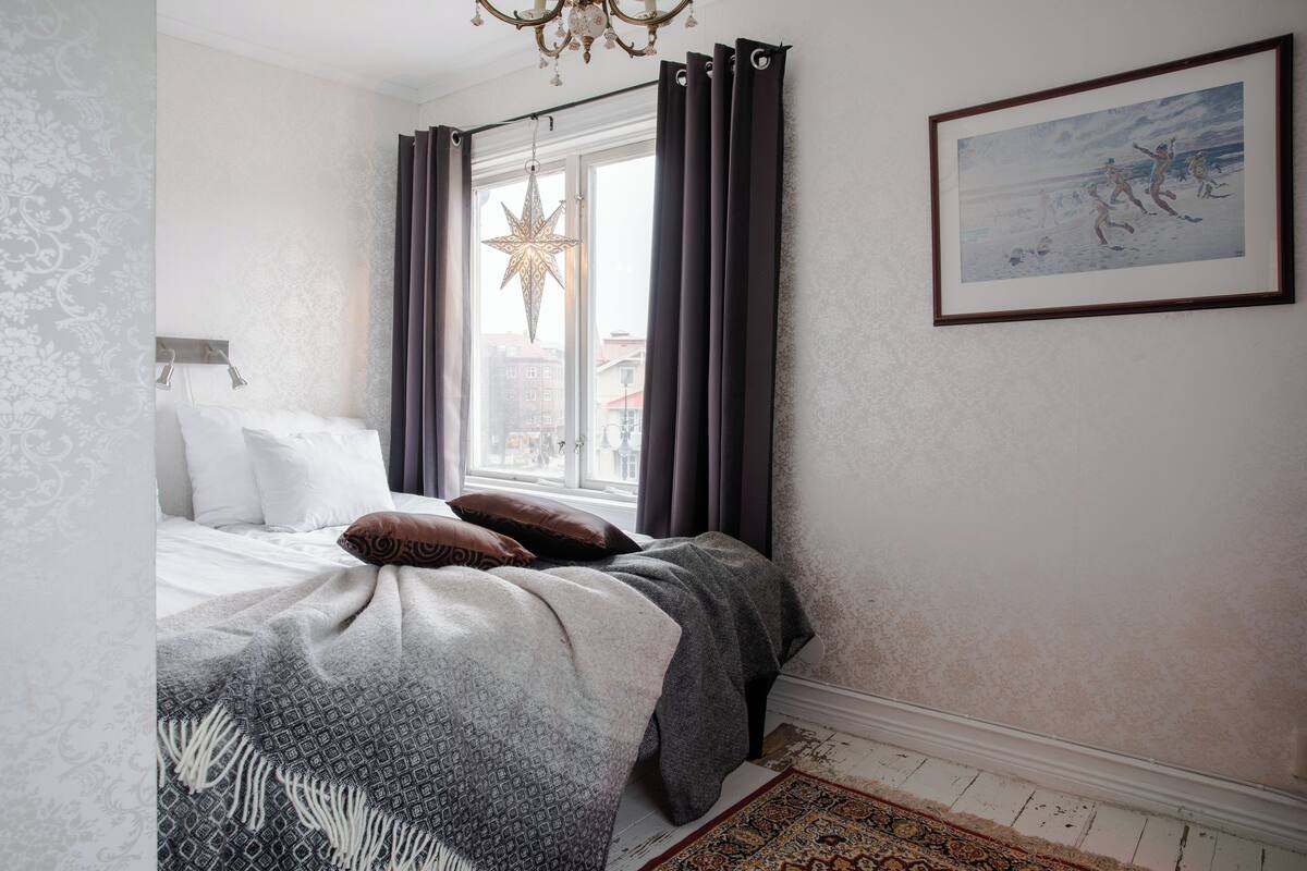 Une chambre à coucher avec un lit, une décoration en forme d’étoile, un tableau encadré et une fenêtre avec des rideaux.
