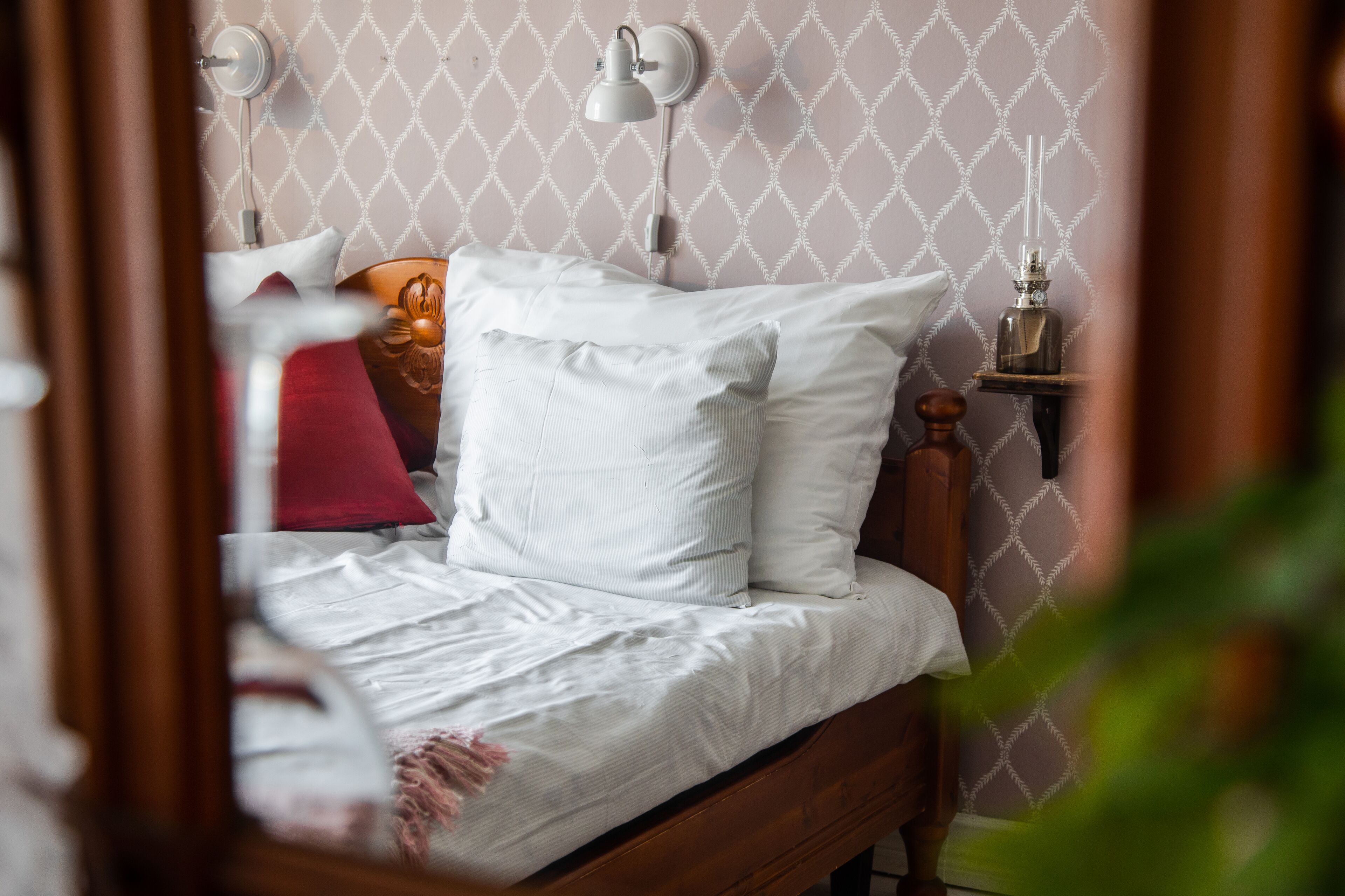 Una cama bien tendida con sábanas blancas, cabecera de madera y una lámpara fijada a la pared.